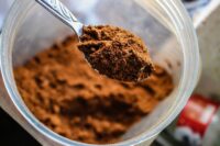 En metallsked fylld med brunt pulver hålls över en plastbehållare.